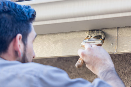 Professional Painter Using A Brush to Paint House Fascia Under Rain Gutter.