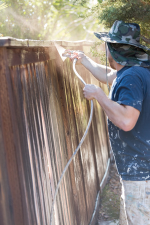 Professional Painter Spraying House Yard Fence with Wood Stain.の写真素材