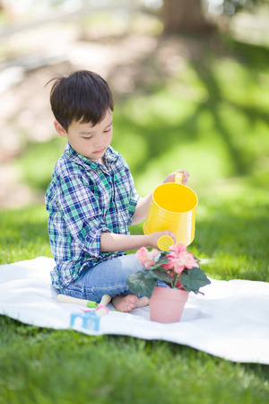 Mixed Race Young Boy Watering His Potted Flowers Outside On The Grassの写真素材