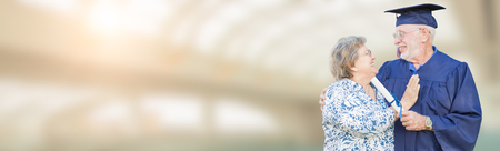 Banner of Senior Adult Male Graduate In Cap and Gown Being Congratulated By Wife Inside School Building.の写真素材