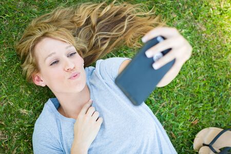 Young Adult Woman Laying in Grass Taking a Selfie with Her Smart Phone.の写真素材