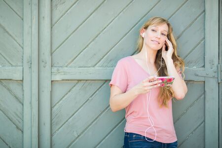 Outdoor Portrait of Young Adult Brown Eyed Woman Listening To Music with Earphones on Her Smart Phone.の写真素材