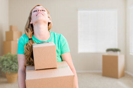 Tired Young Adult Woman Holding Moving Boxes In Empty Room In A New House.
