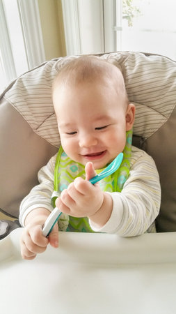 Adorable Chinese and Caucasian Baby Boy Playing With His Spoon Sitting in High Chair.