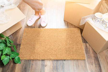 Woman in Pink Shoes and Sweats Standing Near Home Sweet Home Welcome Mat, Boxes and Plant.の写真素材