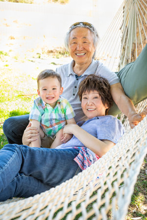 Chinese Grandparents In Hammock with Mixed Race Child.
