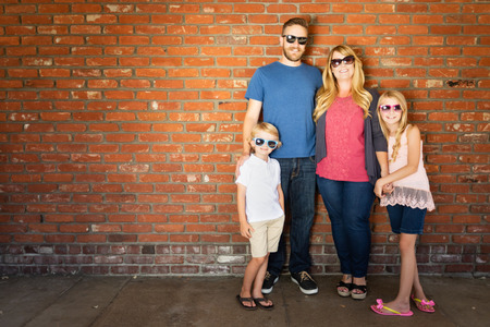 Young Caucasian Family Wearing Sunglasses Against Brick Wall.の写真素材
