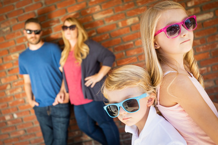 Cute Young Caucasian Brother And Sister Wearing Sunglasses with Parents Behind.の写真素材