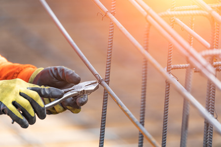 Worker Securing Steel Rebar Framing With Wire Plier Cutter Tool At Construction Site.の写真素材