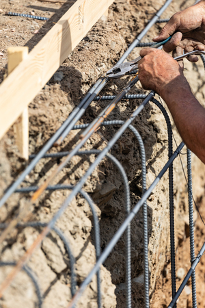 Worker Securing Steel Rebar Framing With Wire Plier Cutter Tool At Construction Site.の写真素材