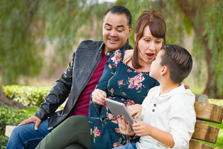 Caucasian Mother and Hispanic Father Using Computer Tablet With Mixed Race Son Outdoors.の写真素材