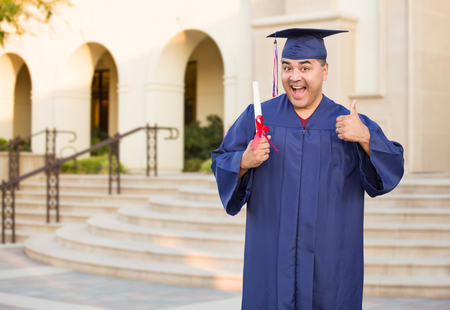 Hispanic Male With Deploma Wearing Graduation Cap and Gown On Campus.の写真素材