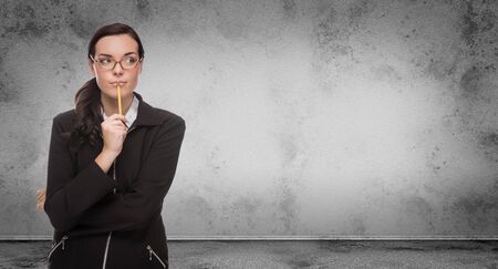 Young Adult Woman with Pencil and Glasses Standing In Front of Blank Grungy Blank Wall with Copy Space.の写真素材