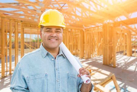 Hispanic Male Contractor with Blueprint Plans Wearing Hard Hat At Construction Site.の写真素材
