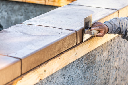 Construction Worker Using Stainless Steel Edger On Wet Cement Forming Coping Around New Pool.