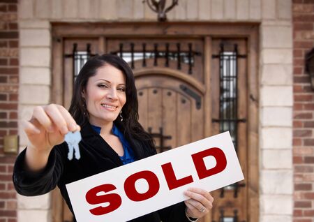 Hispanic Woman Holding Sold Sign and Keys In Front of House.の写真素材