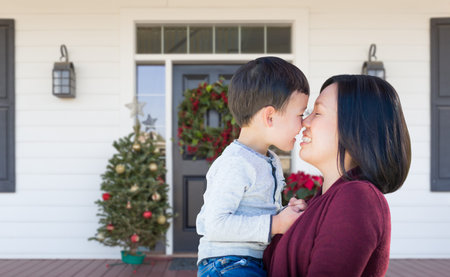 Chinese Mother and Mixed Race Child Rubbing Noses Standing on Christmas Decorated Front Porch.