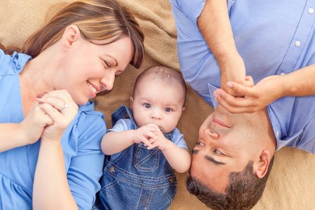 Young Mixed Race Couple Laying With Their Infant On A Blanket.