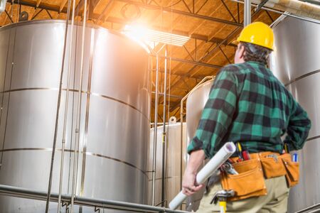 Man Wearing Hard Hat Looking Up At Large Industrial Tanks.の写真素材