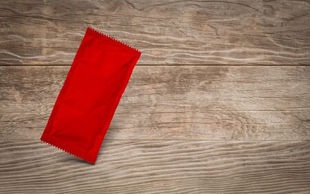 Blank Red Condiment Packet Floating on Aged Wood Background.の写真素材