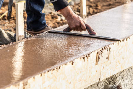 Construction Worker Using Wood Trowel On Wet Cement Forming Coping Around New Pool.の写真素材