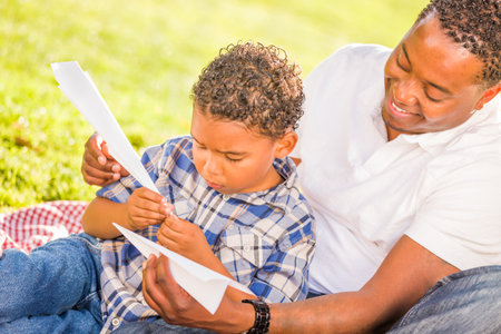 Happy African American Father and Mixed Race Son Playing with Paper Airplanes in the Park.の写真素材