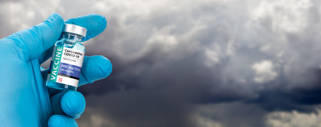 Doctor or Nurse Holding Coronavirus COVID-19 Vaccine Vial Against Stormy Clouds Background Banner.の写真素材