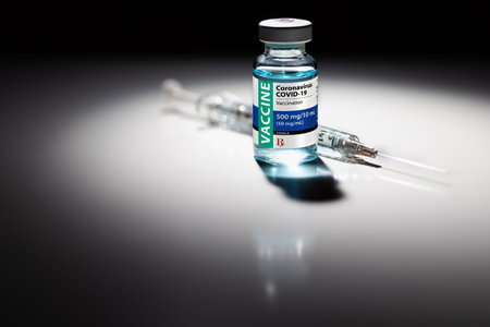 Coronavirus COVID-19 Vaccine Vial and Syringe Spot Lit on Reflective Surface.
