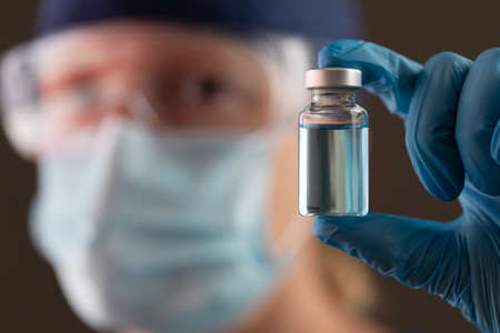 Female Medical Worker Holding Vaccine Vial Wearing Protective Face Mask and Goggles.の写真素材