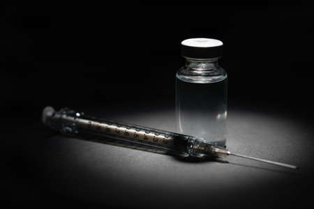 Syringe Needle and Medicine Vaccine Vial Spot Lit on Dark Background.の写真素材