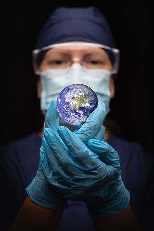 Nurse or Doctor Wearing Face Mask and Surgical Gloves Holding the Planet Earth.の写真素材