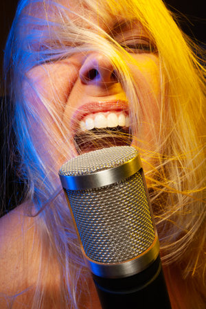 Female vocalist under gelled lighting sings with passion into condenser microphone.の写真素材