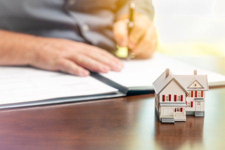 Man signing real estate contract papers with small model home in front