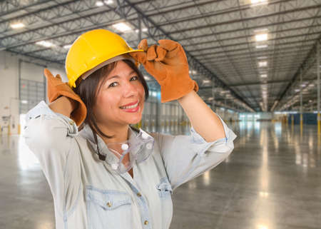 Hispanic Female Contractor Wearing Hard Hat Standing in Empty Industrial Warehouse.の写真素材