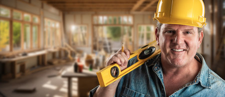 Happy Male Contractor at a Construction Site Wearing a Hard Hat and Work Gloves Holding His Level.