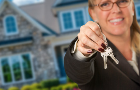 Female Real Estate Agent Presenting House Keys In Front of New House. Focus is on the Keys.の写真素材