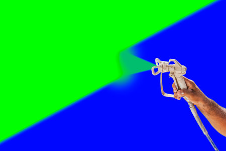 Professional Spray Painter Holding Spray Gun Spraying Surface Against Green and Blue Screen Chroma Key Background.の写真素材