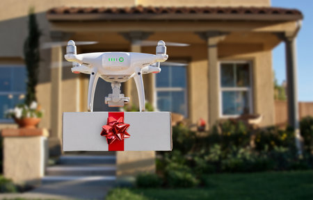 Unmanned UAV Quadcopter Drone Delivering Box With Red Bow and Ribbon To House.の写真素材