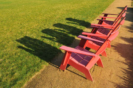 Three chairs sit on a path in the sun near a grass field area.の写真素材