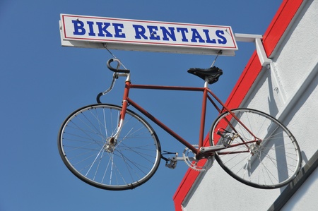 Bike rental sign with a bike haning from it next to a building のeditorial素材