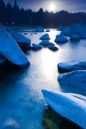 The moon reflects on the water between large boulders in the lakeの写真素材