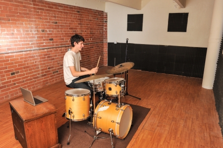 Drummer playing drums in a brick walled studio with computer on chairの写真素材
