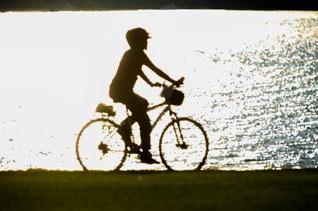 A bike rider silhouette by the water on a path near a fieldの写真素材