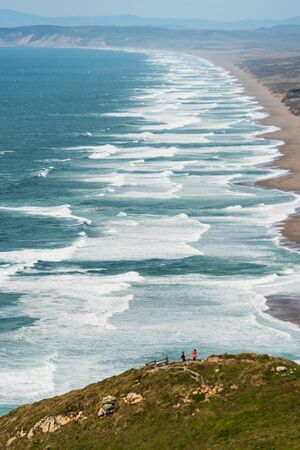 Pacific Ocean waves crash below a cliff with a wooden fenceの写真素材