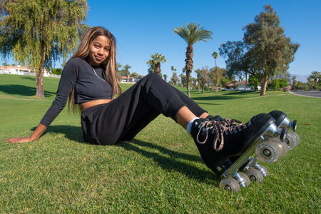 Woman with long hair and wearing roller skates sits on the grass