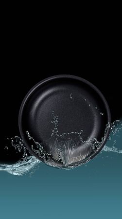 Black dishes plate in spray of water, on a black background.の写真素材