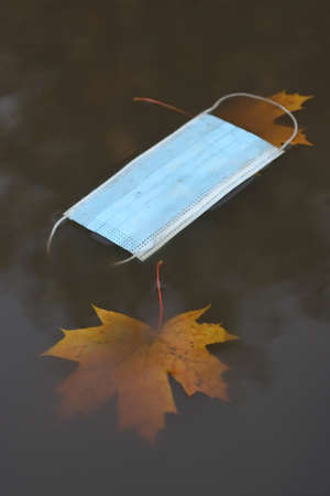 Discarded medical mask for viral infections, floats in an autumn puddleの写真素材