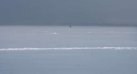 A lone fisherman, fishing in the winter on a frozen bay.の写真素材