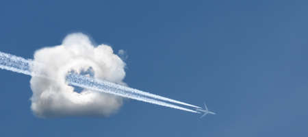 An airplane flying through a cloud in the form of a camera against a blue sky.の写真素材