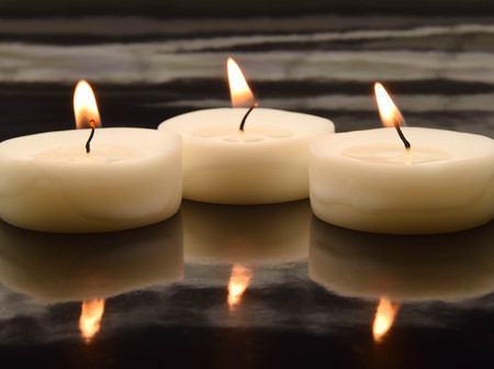 three small tea lights on a black, mirroring surfaceの写真素材